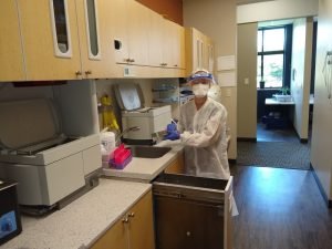 Dental Technician with Face Shield and Mask Working in Facility Beside Sink